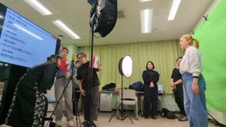 手話CG映像収録の様子です。学生らが撮影スタッフを務め、大型モニターに出されたテキストをもとに、モデルの学生が手話を表現します。