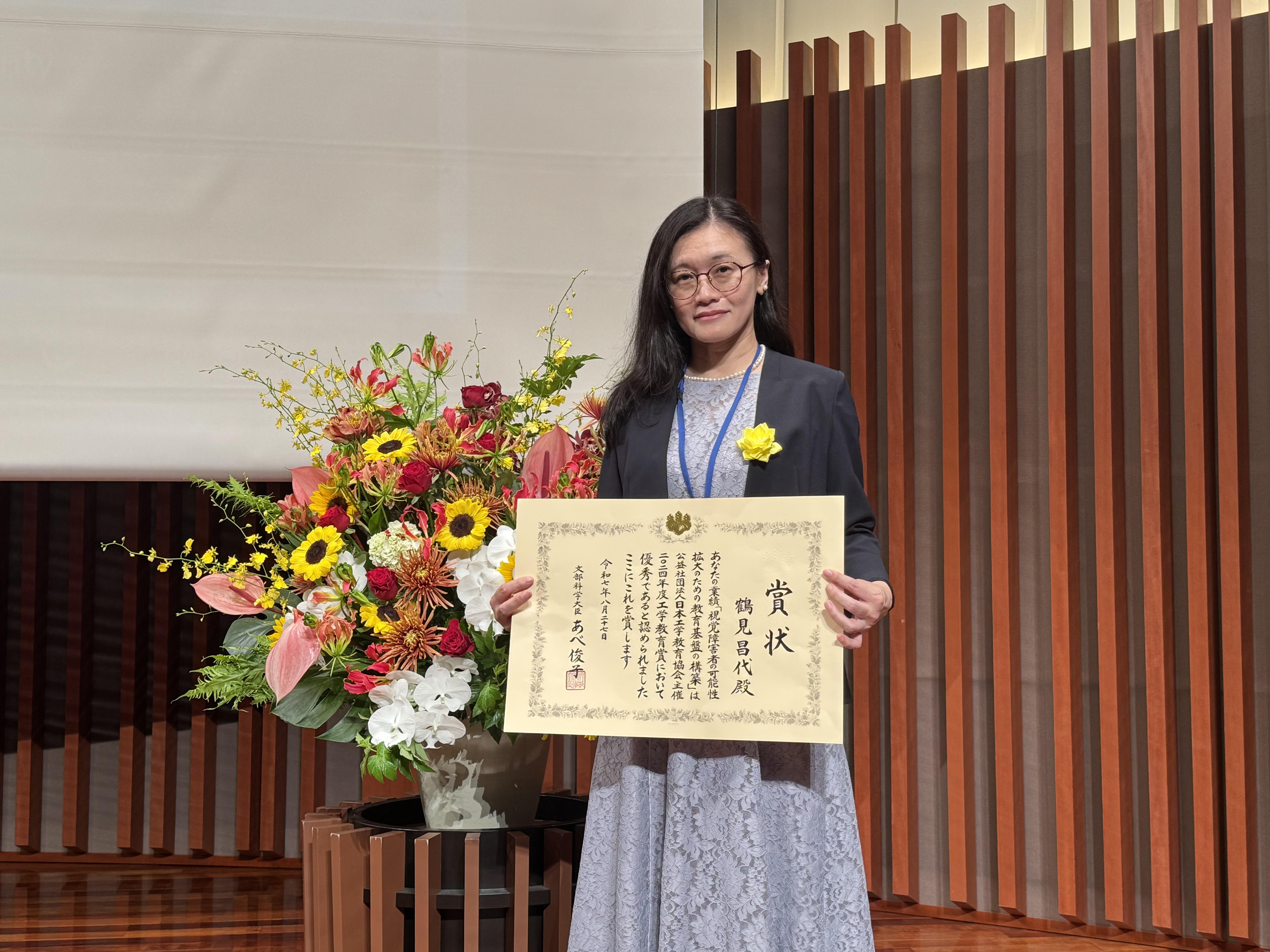 賞状を持って立っている鶴見准教授