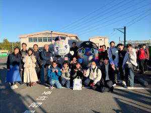 TXのマスコットキャラクターであるユニールとスピーフィを中央に、本学関係者が集合している様子